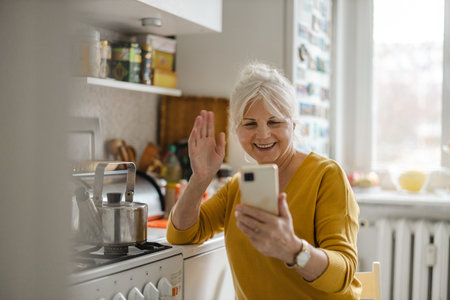 Portrait of happy senior woman using mobile phone in kitchen at homeの写真素材