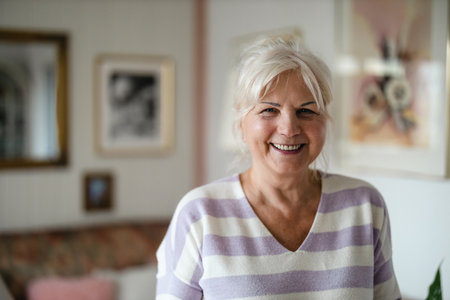 Portrait of happy senior woman smiling at camera in living room at homeの写真素材