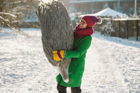 Happy woman carrying the Christmas tree outdoorsの写真素材