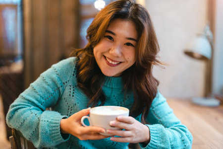 Portrait of smiling young woman holding cup of coffee at coffee shopの写真素材