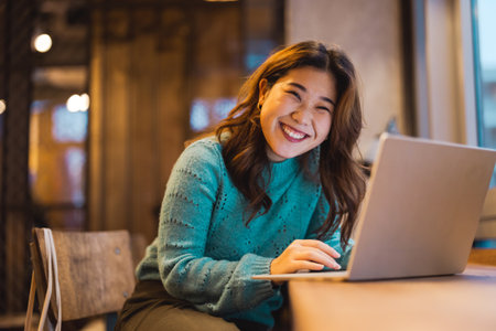 Portrait of smiling young woman using laptop while sitting at table in cafeの写真素材