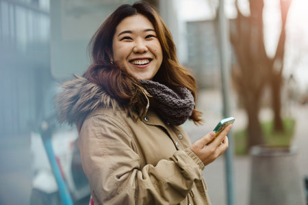 Smiling asian woman using mobile phone outdoors in the city.の写真素材