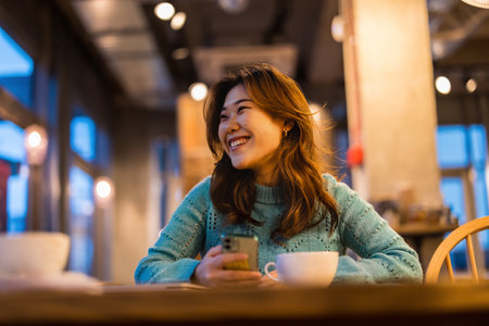 Young woman using mobile phone in a cafe at night, asianの写真素材