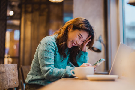Young woman using mobile phone and laptop in coffee shop. Freelance business concept.の写真素材