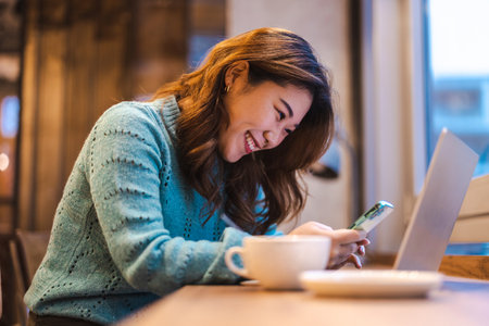 Portrait of young woman using mobile phone and laptop in coffee shopの写真素材
