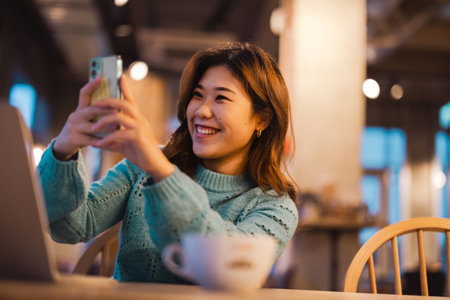 Woman taking a selfie with her mobile phone in a cafe at nightの写真素材