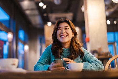 Portrait of smiling asian woman drinking coffee in cafe at nightの写真素材
