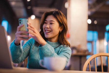 Portrait of smiling asian woman using mobile phone in coffee shopの写真素材