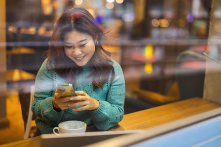 Portrait of young woman using mobile phone while sitting at table in cafeの写真素材