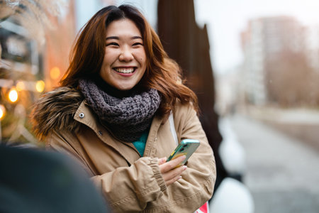 Portrait of a smiling young asian woman using mobile phone outdoorsの写真素材
