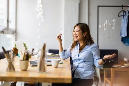 Portrait of smiling businesswoman sitting at table in office and looking awayの写真素材