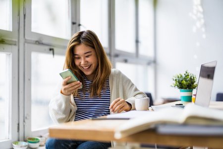 Portrait of a smiling businesswoman using mobile phone while sitting at office deskの写真素材