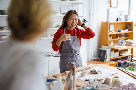 Smiling female ceramist looking at her colleague in her workshopの写真素材