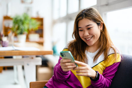 Smiling young asian woman using mobile phoneの写真素材