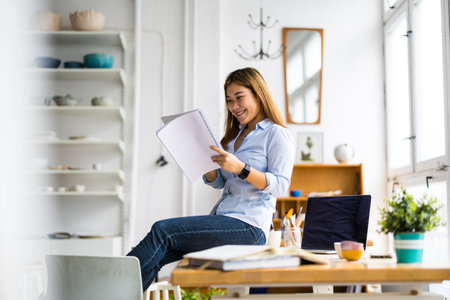 Young businesswoman sitting on the desk at office and writing in notebookの写真素材