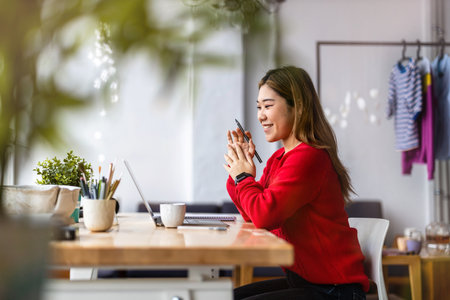 Smiling businesswoman using mobile phone while sitting at her desk in officeの写真素材