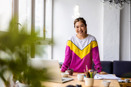 Smiling asian woman working on laptop at desk in creative officeの写真素材