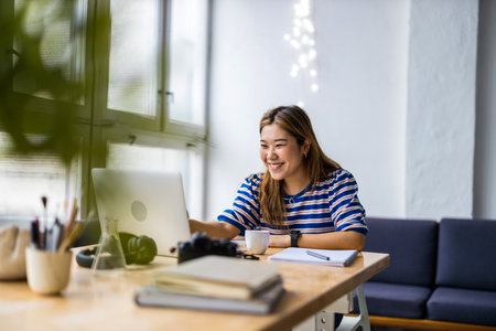 Portrait of a smiling young businesswoman working on laptop computer while sitting in officeの写真素材