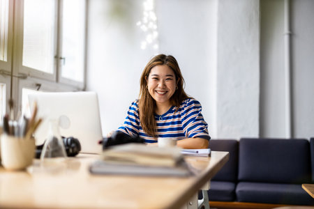 Portrait of a smiling young businesswoman sitting at desk in officeの写真素材