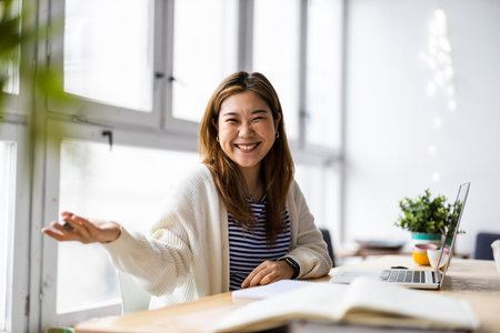 Portrait of smiling young Asian businesswoman sitting at desk in officeの写真素材