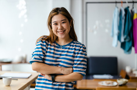 portrait of smiling young asian businesswoman standing with crossed arms in officeの写真素材