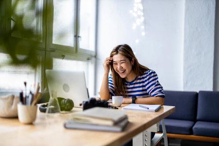 Portrait of happy businesswoman laughing while working on laptop in officeの写真素材
