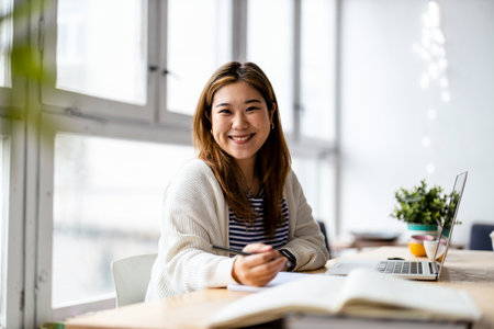 Portrait of smiling asian businesswoman sitting at desk in officeの写真素材