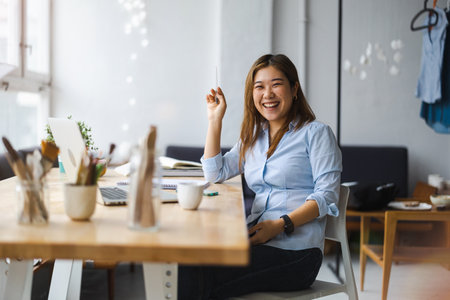 Portrait of smiling asian businesswoman sitting at desk in officeの写真素材