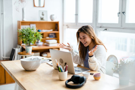 Happy young woman using laptop while sitting at the tableの写真素材