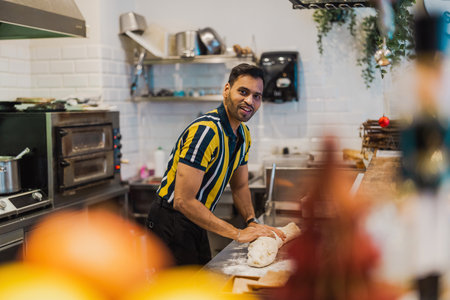 Portrait of smiling male chef kneading dough in commercial kitchenの写真素材