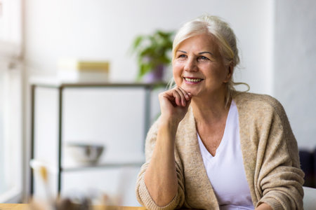 Portrait of happy senior woman sitting at table in kitchen at homeの写真素材