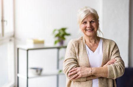 Portrait of smiling senior woman standing with arms crossed in living roomの写真素材