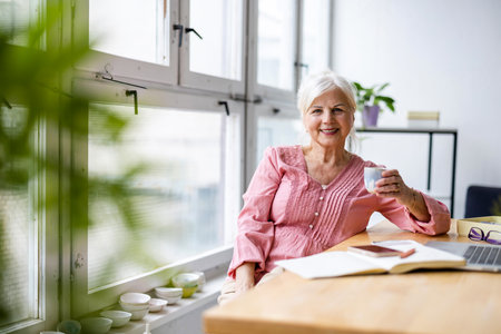 Smiling senior woman sitting at the table and holding cup of coffeeの写真素材
