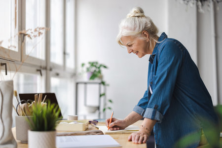 Side view of young female designer writing in notebook while working in creative officeの写真素材
