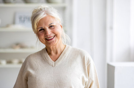 Portrait of smiling senior woman looking at camera while standing at homeの写真素材