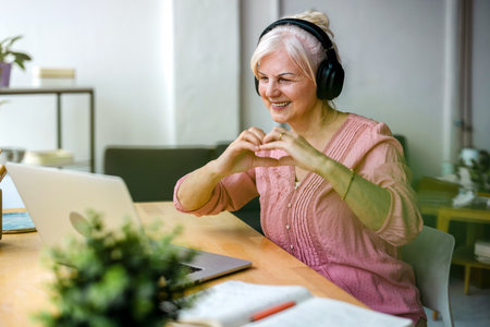 Senior woman using laptop and listening to music in her living room at homeの写真素材