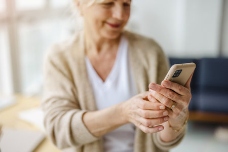 Close up of senior woman using mobile phone while sitting at table in officeの写真素材