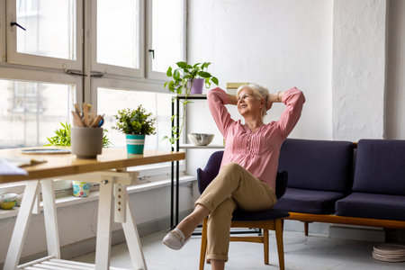 happy senior woman sitting on sofa and stretching in living room at homeの写真素材