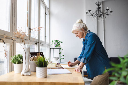 side view of mature businesswoman drawing in notebook at workplace in officeの写真素材