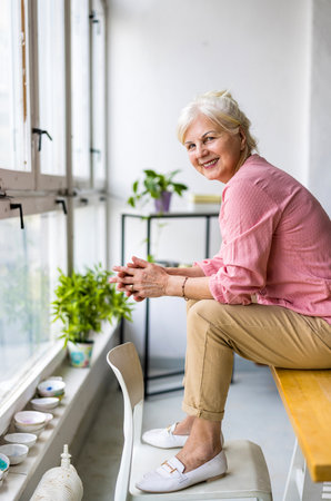 senior woman sitting on chair and smiling at camera in kitchen at homeの写真素材