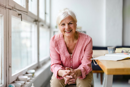 Portrait of smiling senior woman sitting at table in cafe and looking at cameraの写真素材