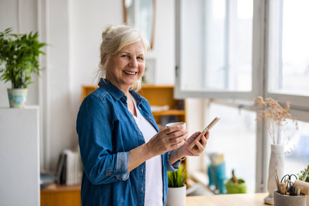 smiling senior woman with cup of coffee and smartphone in modern officeの写真素材
