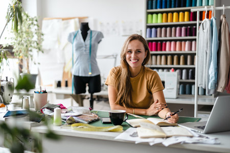 Smiling fashion designer sitting at her desk in her studio and looking at cameraの写真素材