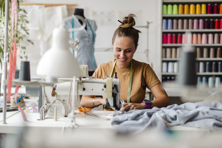 Fashion designer woman working on her designs in the studio, she is using a sewing machineの写真素材
