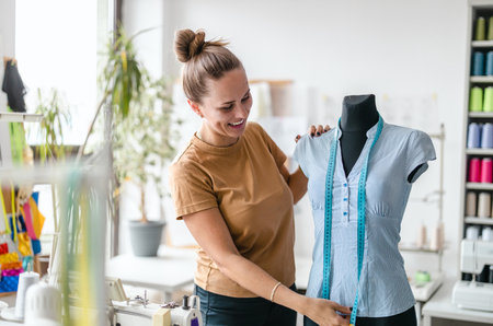portrait of smiling fashion designer measuring mannequin in sewing studioの写真素材