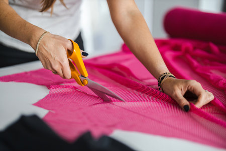 Fashion designer woman working on her designs in the studio, she is cutting fabric