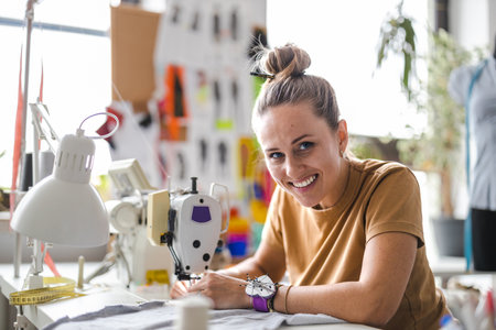 Portrait of smiling female fashion designer sitting at her desk in studioの写真素材