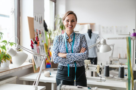 Portrait of a smiling female fashion designer standing with arms crossed in sewing studioの写真素材