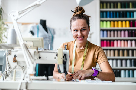 Portrait of smiling female fashion designer working with sewing machine in studioの写真素材