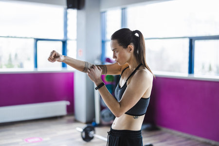 Woman doing arm curl exercise in fitness studio. Side view of female athlete in sportswear working out at gym.の写真素材